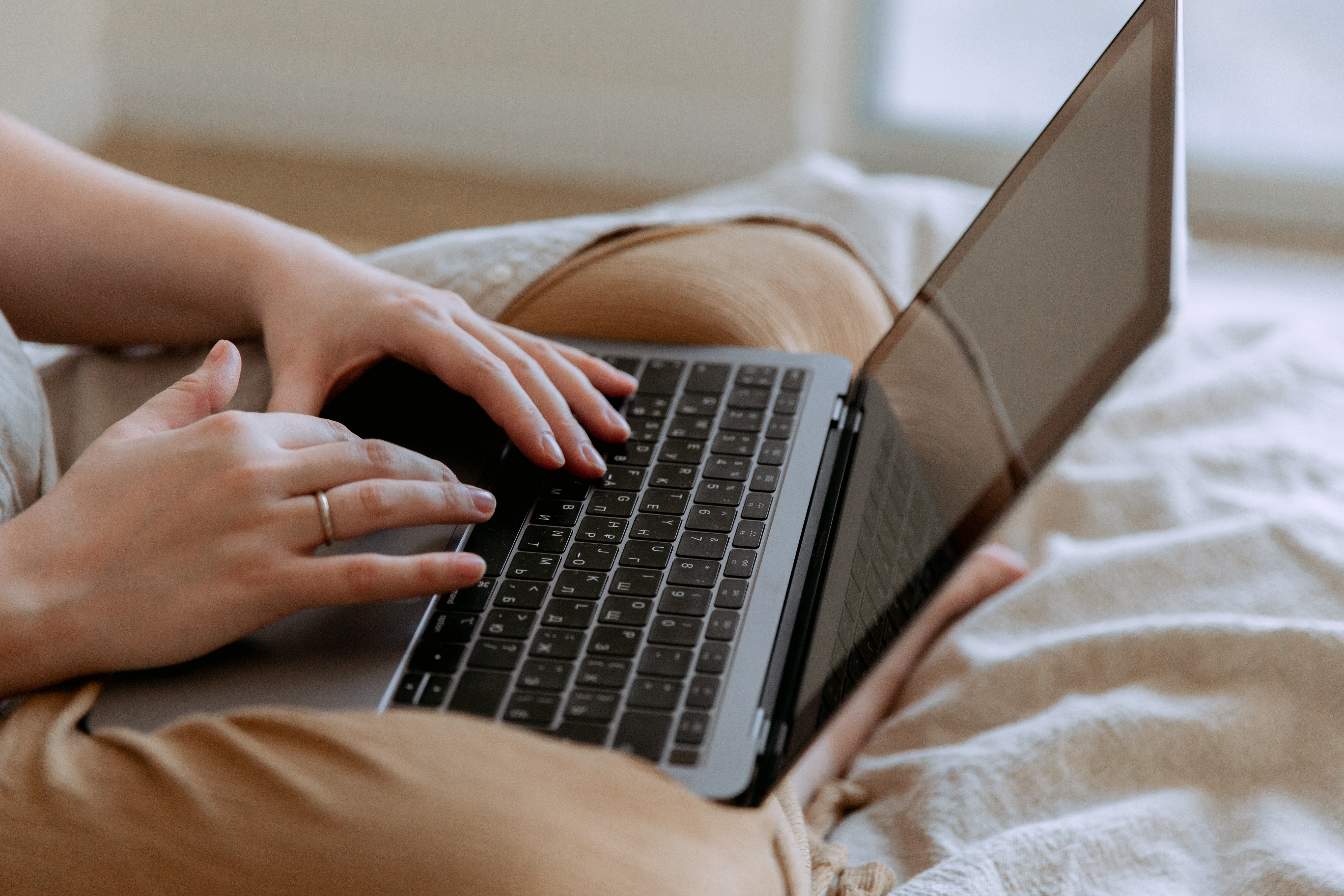 Faceless woman using a laptop while sitting on a bed.