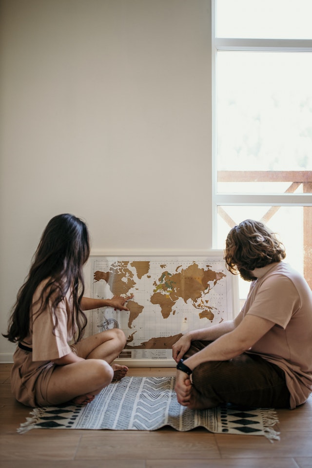 A woman and a man sitting on the floor looking as she points to a location on a map using latitude and longitude coordinates.