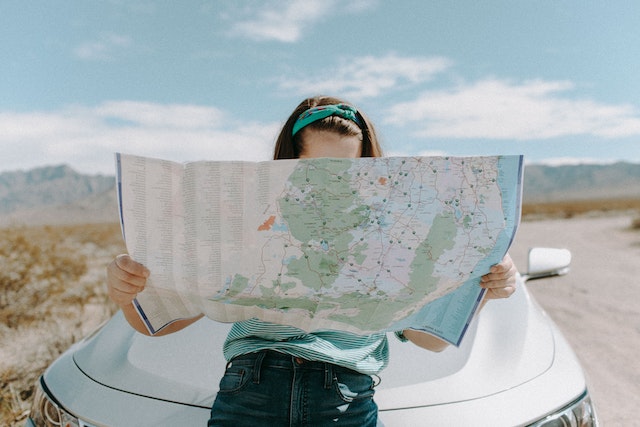 A lady in front of her car checking a physical map to determine her route.