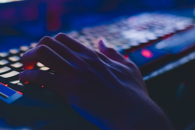 Person's hand typing on a glowing computer keyword in the dark.