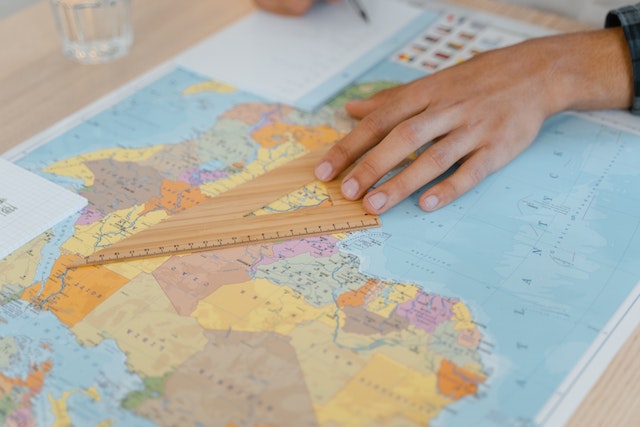 A person practicing geo-mapping by taking notes and measuring distance on a physical map.