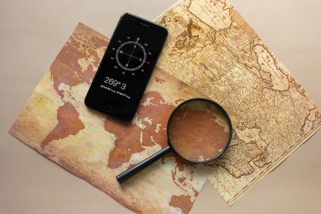 A smartphone displaying coordinates on top of two physical maps