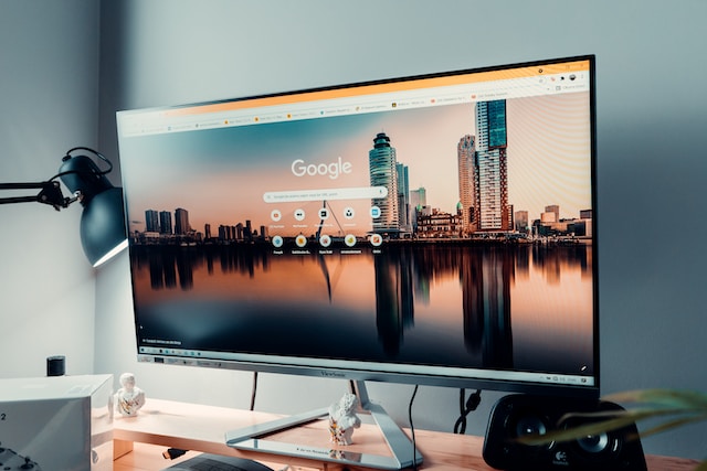 Large computer display in a home office showing the Google home page with a skyline background
