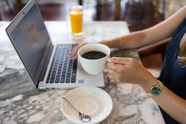 Unseen woman holding a coffee cup while googling on her computer at a coffeeshop.