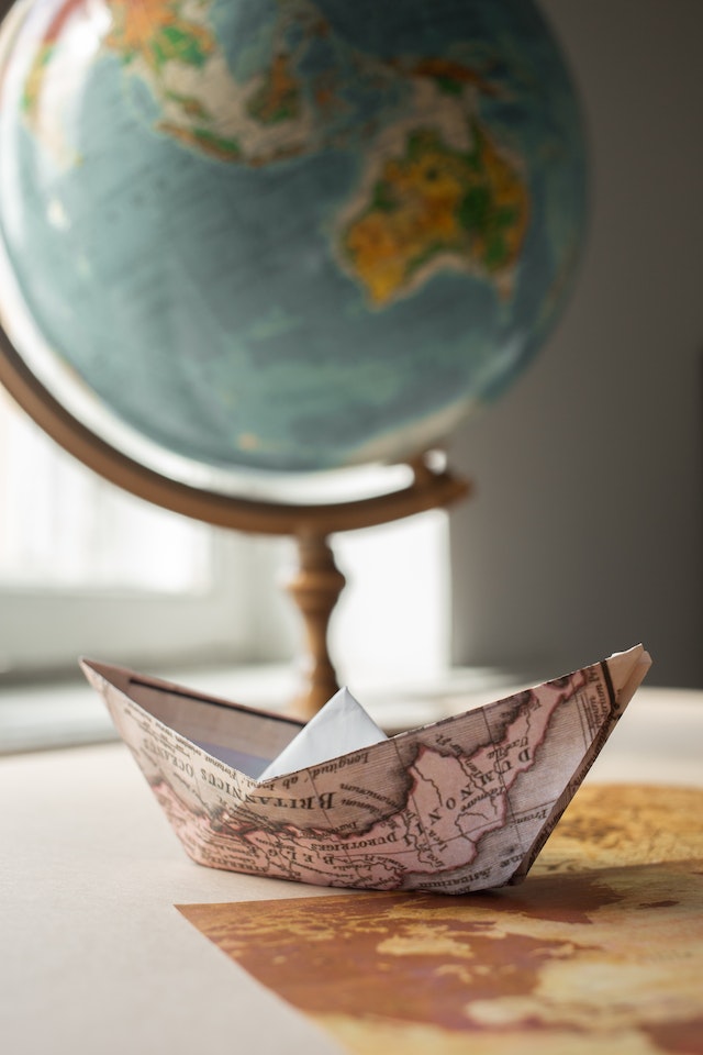 Paper boat folded from a map with labeled bodies of water next to a globe.