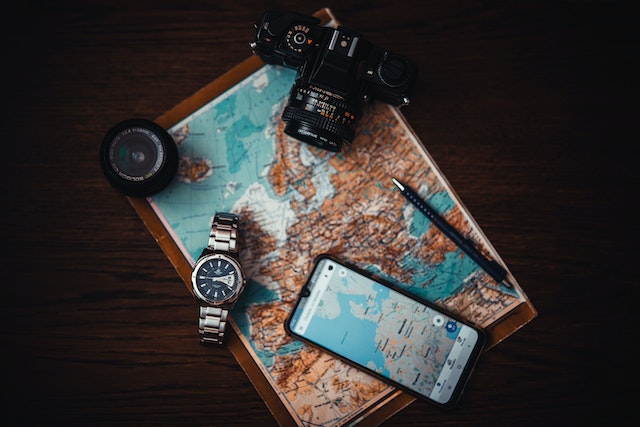 Tools of navigation: A digital camera, smartphone, wristwatch, compass, pen, and a physical map.  