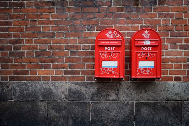 Two red post boxes mounted on a brown concrete wall.
