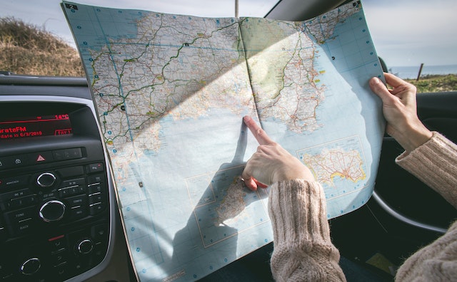 A lady in her car utilizing a physical map to ascertain her current location and next stop.