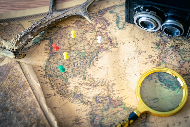 A physical map with pins as well as a magnifying lens and digital camera on it. 
