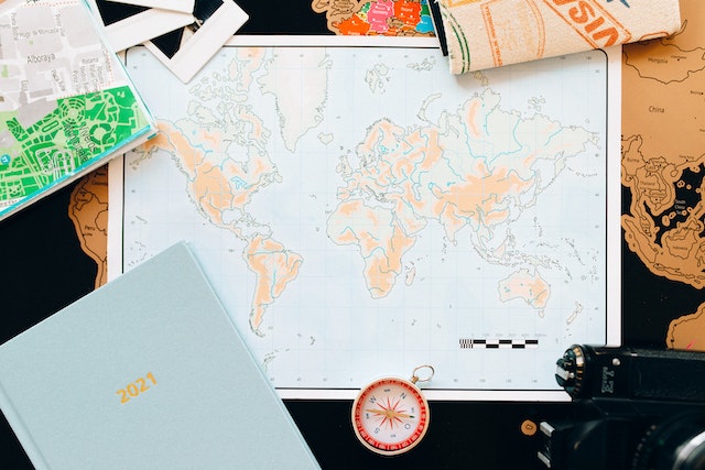 A physical world map, compass, and a journal on a table.