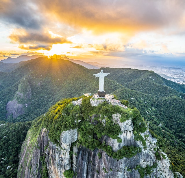 A wide sunrise view of the Christ the Redeemer statue on a mountain top in Brazil.